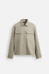Sobrecamisa color arena de corte recto, con cuello solapa, cierre frontal con cremallera, manga larga con puños abotonados, dos bolsillos de plastrón con solapa en el pecho y dos bolsillos laterales en la costura de la cadera.