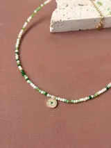 Collar corto de cristalitos facetados en tonos verdes y blancos, con dije redondo con forma de ojo turco con circonia verde en el centro, con baño de oro.