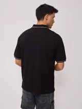 Remera polo negra de corte regular, con cuello y mangas con rayas en contraste blancas y logo bordado en el pecho.