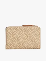Billetera plegable color beige con estampado del logo de Tommy Hilfiger en toda la superficie. Tiene cierre de cremallera, múltiples ranuras para tarjetas, compartimento para billetes y bolsillo exterior para monedas.