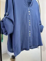 Blusa azul jeans de manga larga regulable, con escote en pico y botones en la parte delantera.