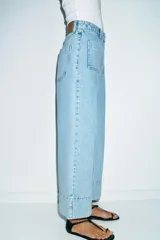 Jeans de tiro alto con corte wide leg cropped, confeccionados en denim de lavado claro. Presentan costuras marcadas en el frente, bolsillos de plastrón delanteros y cierre frontal con cremallera y botón.