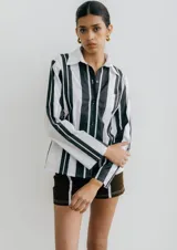 Camisa blanca con rayas verticales negras, de manga larga y corte recto. Tiene cuello clásico, cierre con botones y bolsillo en el pecho.