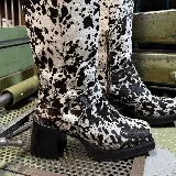 Bota de caña alta con estampado animal print en blanco y negro, con cierre lateral y hebilla decorativa.