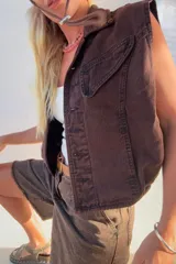 Chaleco vintage de jean color marrón oscuro, con cuello solapa, cierre frontal con botones metálicos, bolsillos delanteros con solapa y corte oversize.