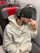 Buzo canguro con capucha, color blanco con estampado de camuflaje en tonos grises. Estampado en la espalda con el logo de la marca y nombres de ciudades.