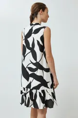 Vestido corto sin mangas, con cuello en V y estampado abstracto en blanco y negro. Tiene cierre frontal con botones y volado en el ruedo.