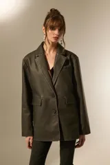 Blazer de eco-cuero color verde oliva oscuro, con efecto lavado, corte holgado, cuello solapa y dos botones frontales. Presenta pespuntes contrastantes y bolsillos de parche.