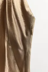 Vestido midi color dorado, con cuello halter ajustable con botón y hombros descubiertos. Detalle de tejido efecto arrugado, espalda pronunciada, bajo asimétrico y cierre lateral con cremallera oculta.