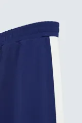 Pantalón deportivo azul marino con paneles laterales blancos y detalles en azul eléctrico. Corte relaxed fit, cintura elástica ajustable con cordón, bolsillos frontales ocultos y puños elásticos.