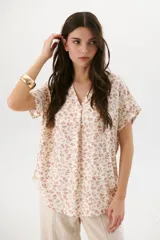 Blusa estampada color crema con hojas marrones, escote en V y mangas cortas.
