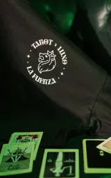 Remera negra de manga corta con cuello redondo y calce oversize. Presenta una estampa en la espalda inspirada en el tarot, con la carta "La Fuerza" que muestra a una mujer desnuda sobre un leopardo, rodeada de vegetación y un sol rojo.