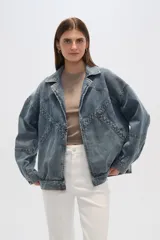 Campera de jean celeste con cuello clásico, solapas, cierre frontal con botones metálicos y mangas largas con puños abotonados. Presenta detalles de costuras diagonales y apliques de tachas metálicas.