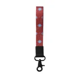 Llavero de muñeca con cinta de tela roja con estampado de estrellas azules y puntos blancos. Incluye un gancho giratorio de metal negro y un detalle de cuero sintético negro con logo grabado.