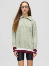 Sweater de punto color verde claro con cuello polo con cierre de cremallera, mangas largas y diseño con trenzas. Puños acanalados con rayas en color borgoña y blanco.
