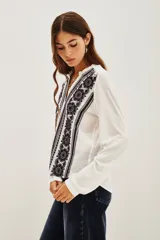 Camisa blanca de manga larga con cuello mao y escote en V, con bordados negros en el frente y puños.