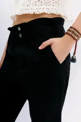 Pantalón negro de tiro alto con elástico interno en la cintura, botones falsos y terminación con volado. Tiene bolsillos aplicados en delantero y falsos en espalda.