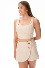 Top corto color beige, con escote cuadrado y breteles anchos. Presenta detalle de elástico fruncido en los laterales.