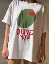 Remera blanca de algodón con estampa de una aceituna verde con un corazón rojo y la frase "Olive You" en rojo.