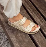 Sandalias de cuero color blanco con estampado de piel de serpiente y hebillas doradas.
