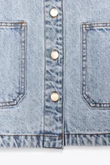 Cazadora de denim verde oliva, con cuello solapa, manga larga, bolsillos delanteros de plastrón y cierre frontal con botones metálicos.