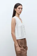 Chaleco sin mangas color blanco crudo, tejido a crochet o punto abierto, con escote en V y cierre frontal mediante lazos cruzados.
