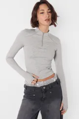 Top manga larga gris de punto roma, con media polera y cuello con cierre de nylon a tono. Mangas con mitones en los puños y estampa de isologo con serigrafía al tono en el delantero.