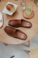 Mules de cuero negro con punta cuadrada y detalle de tachas plateadas en el borde superior.