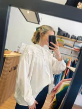 Camisa blanca oversize con detalles de puntilla en el frente y mangas abullonadas.