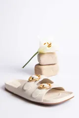 Sandalias de cuero color beige con dos tiras anchas y hebillas doradas ajustables.