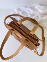 Cartera bandolera de cuero color tostado, con correa larga regulable, bolsillo frontal y forro de tela.