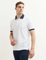 Remera polo blanca de piqué con cuello y puños en azul marino. Tiene tapeta de dos botones y bolsillo de parche en el pecho.