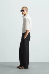 Camisa de corte relajado en color blanco, confeccionada en tejido de algodón con textura de aplicaciones. Posee cuello bowling, manga corta y cierre frontal con botones.