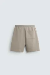 Bermuda color arena de tejido interlock de algodón con elasticidad, corte relaxed fit, cintura elástica ajustable con cordón interior, bolsillos laterales y bolsillo trasero de plastrón.