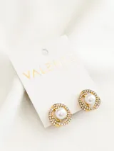 Par de aros dorados con forma circular, con incrustaciones de strass y una perla blanca en el centro.