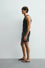 Bañador negro con estampado de dibujos en blanco. Tiene cintura elástica ajustable con cordón, bolsillos laterales y trasero.