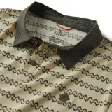 Chomba manga corta color beige con estampado de líneas onduladas en verde oscuro. Tiene cuello polo verde oscuro y logo pequeño en el pecho.