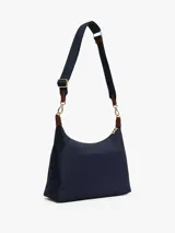 Bolso de hombro tipo hobo de nailon color azul marino, con correa de hombro ajustable de tela azul marino y detalles en cuero marrón. Presenta una franja vertical central con ribetes rojos y blancos, y un monograma TH dorado en el centro.