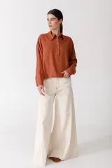 Blusa blanca de lino con cuello polo, manga larga y botones dorados. Presenta costuras a contratono en color naranja.