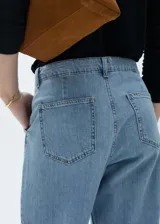 Pantalón de jean celeste de corte recto, tiro medio y largo hasta el tobillo. Presenta cierre de cremallera y botón, trabillas para cinturón y pinzas en la parte delantera.
