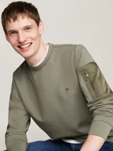 Buzo verde militar de Tommy Hilfiger, de corte clásico con cuello redondo y mangas largas. Presenta un pequeño logo bordado en el pecho y un bolsillo con cremallera en la manga izquierda.