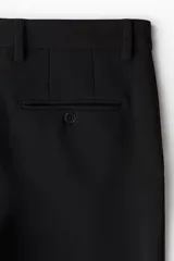 Pantalón negro tobillero con pliegues, corte ajustado, cierre con botón, bolsillos laterales y bolsillos atrás ribeteados con botón.