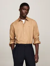 Camisa color beige de corte regular, confeccionada en algodón elástico. Cuenta con cuello abotonado, mangas largas con puños abotonados y logo de Tommy Hilfiger bordado en el pecho.