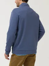 Buzo azul con cuello alto, cierre frontal y logo bordado en el pecho.