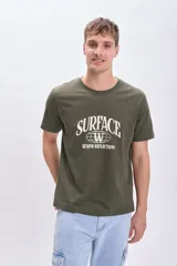 Remera verde militar de manga corta con estampa frontal blanca con la palabra 'Surface' y la frase 'Beyond Reflections'.