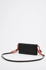 Minibolso negro de estructura blanda con asa de mano de cordón rojo y asa larga extraíble. Presenta logo metálico, acabados metálicos y cierre con botón de presión. Incluye tarjetero interior e interior con logo estampado.