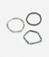 Set de tres pulseras de metal plateado y negro, con diferentes diseños: una de cadena gruesa, una de esferas y una de eslabones.