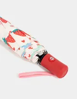 Paraguas corto con funda de tela, estampado con frutillas y corazones. Tiene mango rojo y correa de mano rosa.