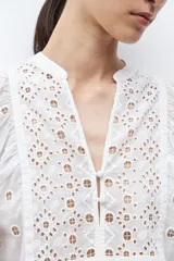 Blusa color verde oliva de manga 3/4 con volumen, cuello mao con abertura en V y botones. Presenta bordados y detalles de broderie calado en el canesú frontal y en las mangas. El cuerpo tiene un corte peplum con frunces.