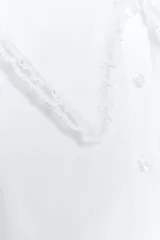 Camisa blanca de popelina de algodón con cuello bobo y mangas largas con elástico en los puños. Detalle de puntilla a tono en cuello y ruedo. Cierre frontal con botones.